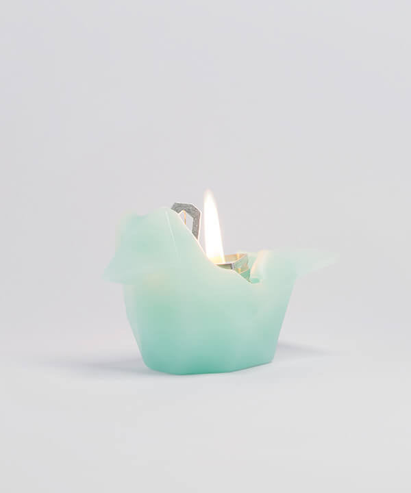 Side view of burning mint bird shaped candle. As the wax melts a metal skeleton frame is revealed. 