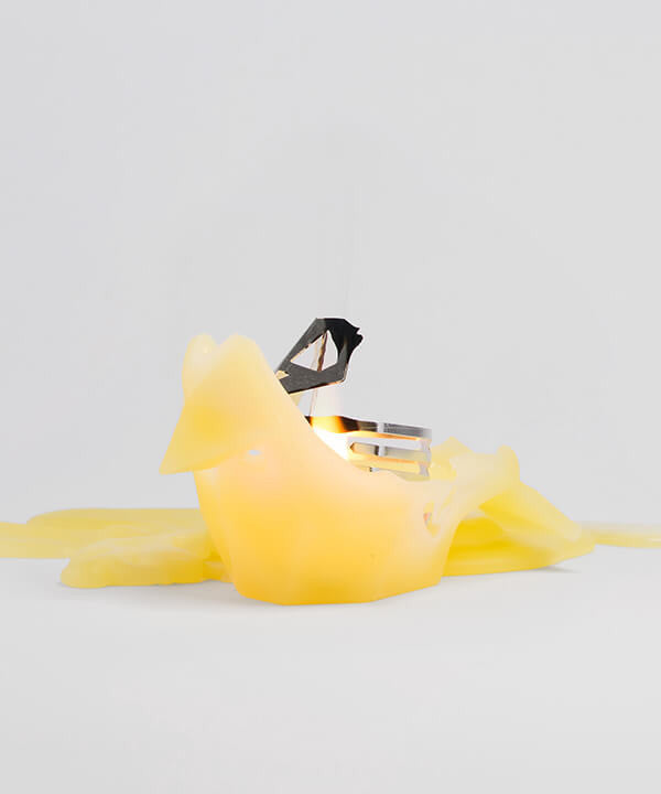 Side view of melted yellow bird shaped candle. When the wick is lit, watch it melt away to reveal a metal skeleton frame. 