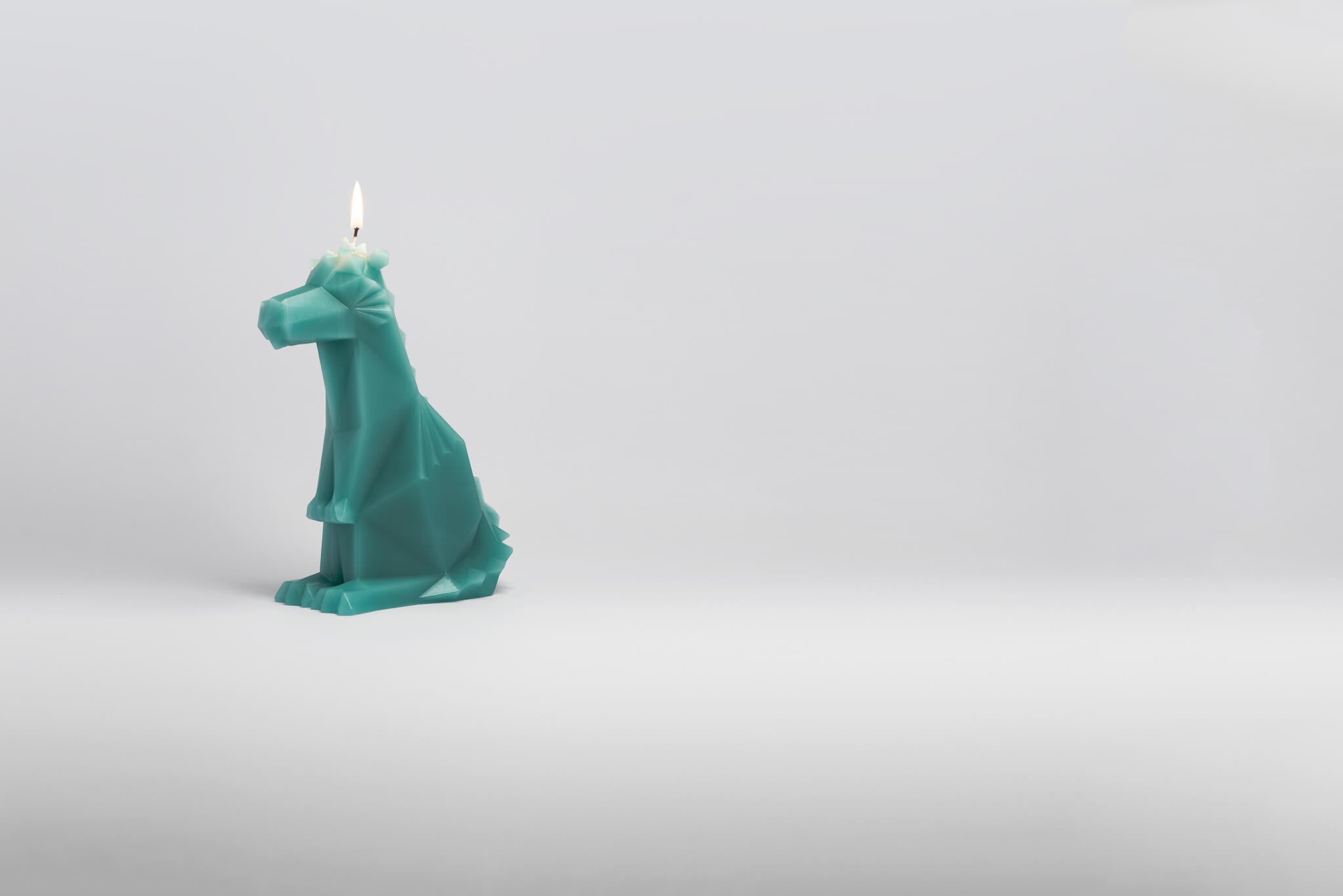 Side view of green dreki the dragon shaped pyropet candle with a burning wick. 