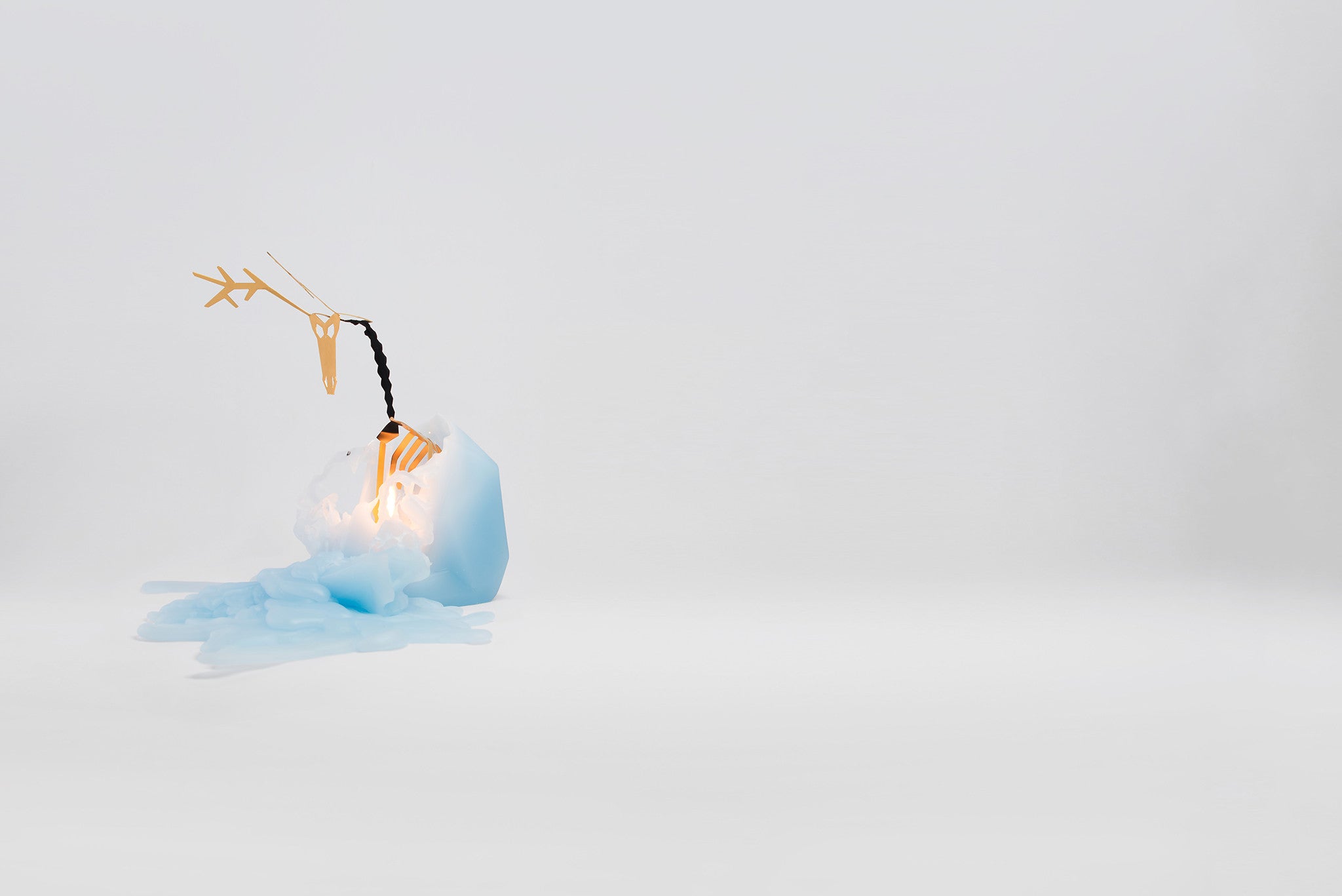 Side view of melting light blue reindeer pyropet candle. As the wax melts, the candle reveals an inner gold skelton frame.