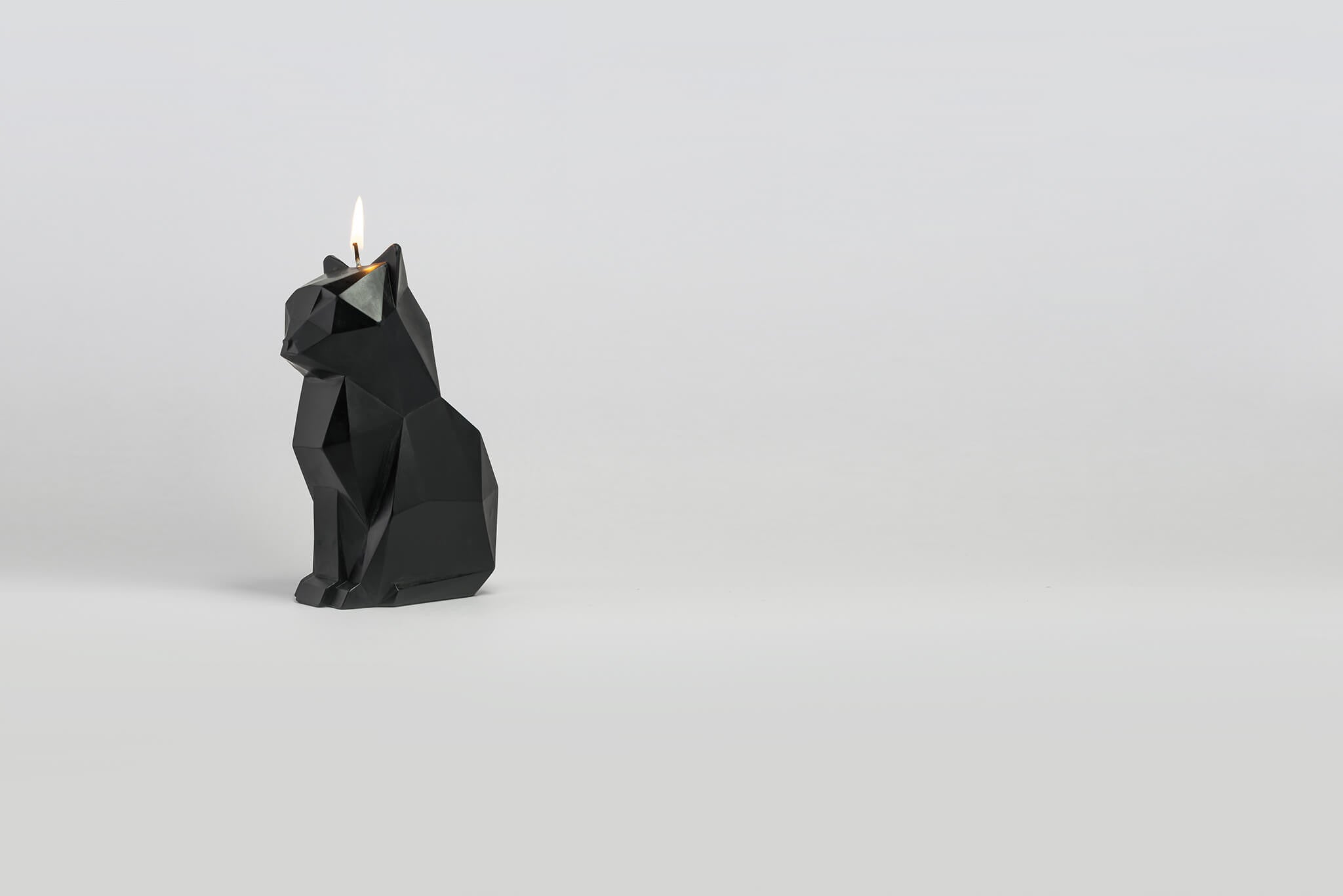 Side view of black kisa the cat candle with a lit wick. 