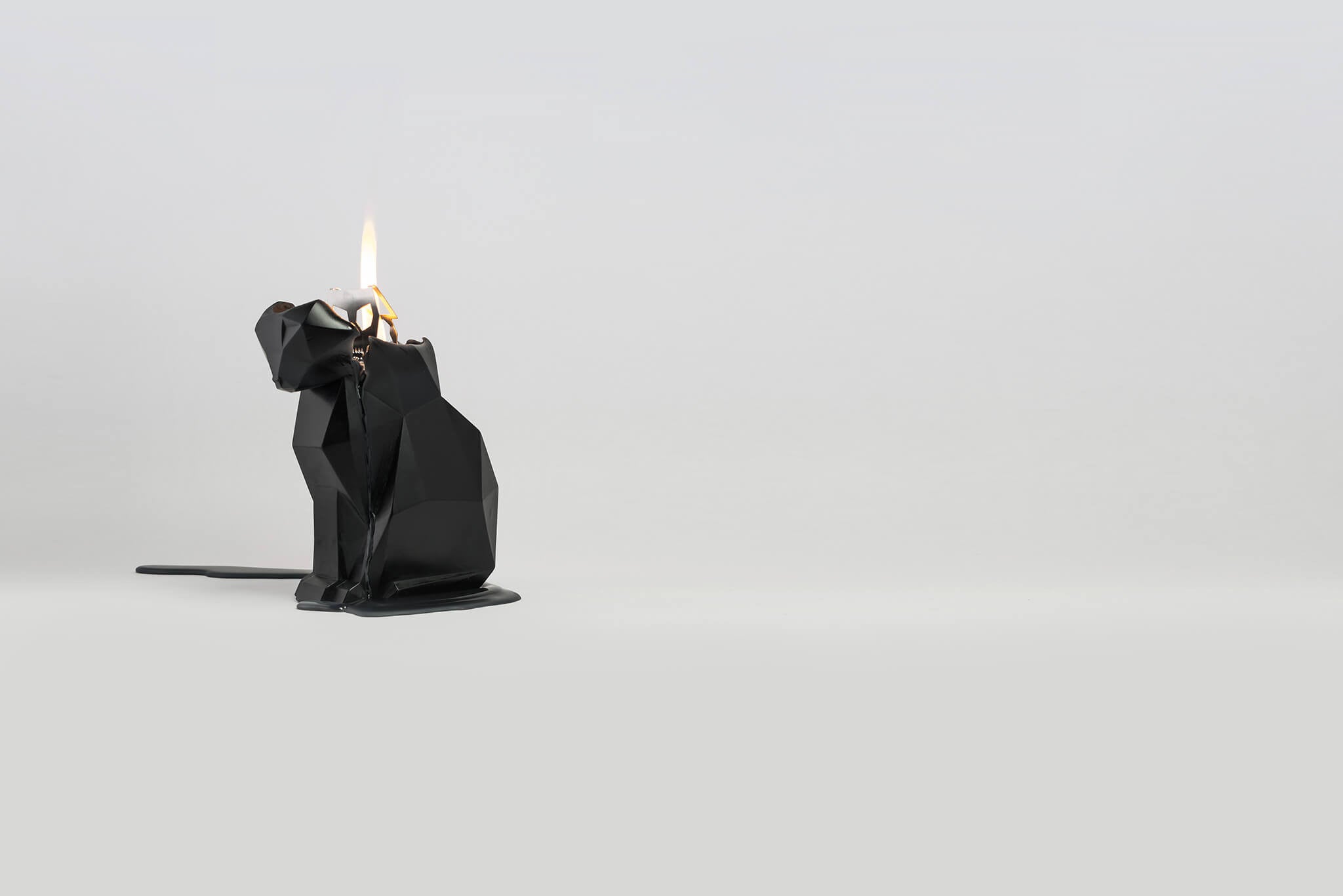 Side view of black kisa the cat shaped candle burning to reveal secret metal skeleton. 