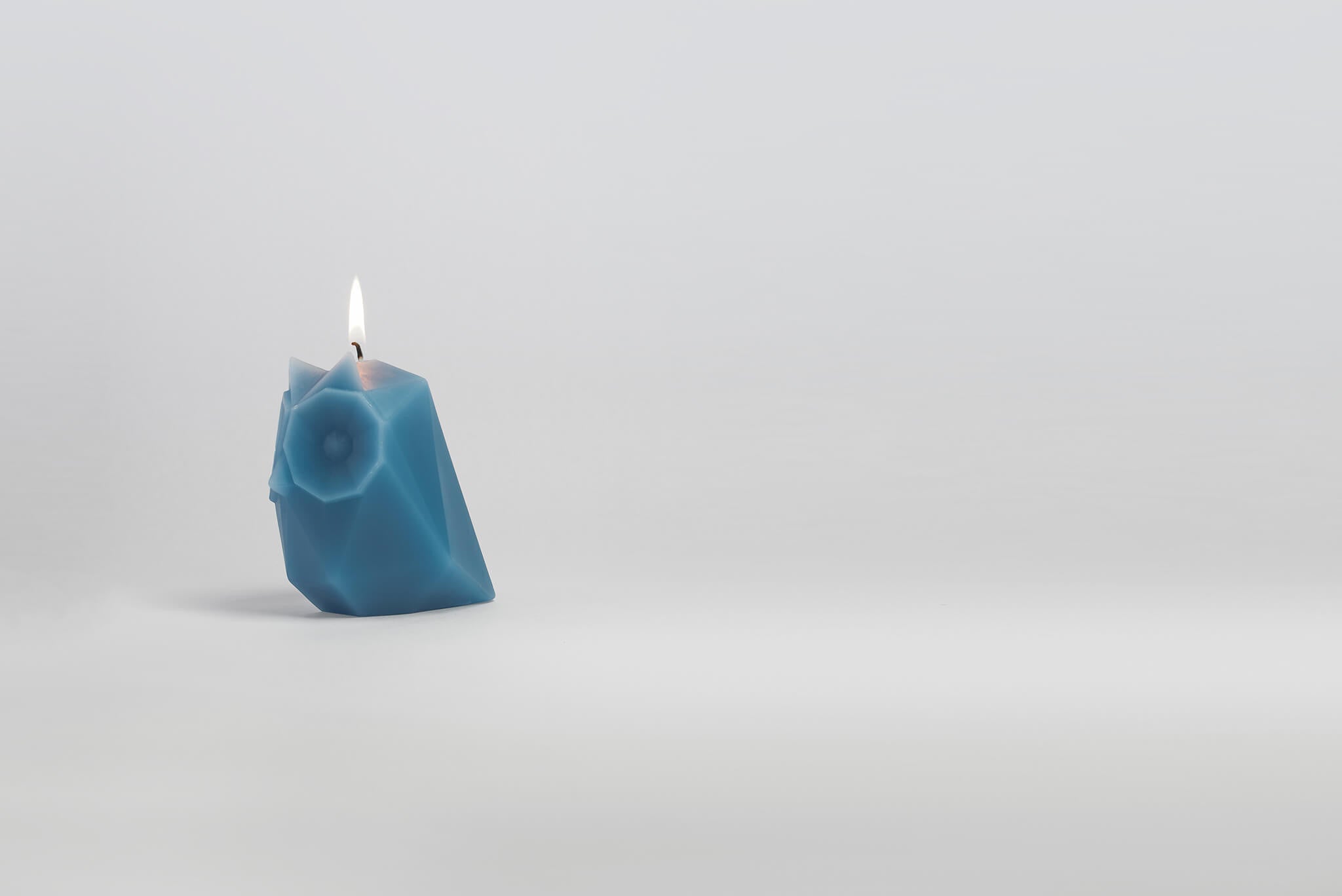 Side view of lit blue owl shaped candle. 