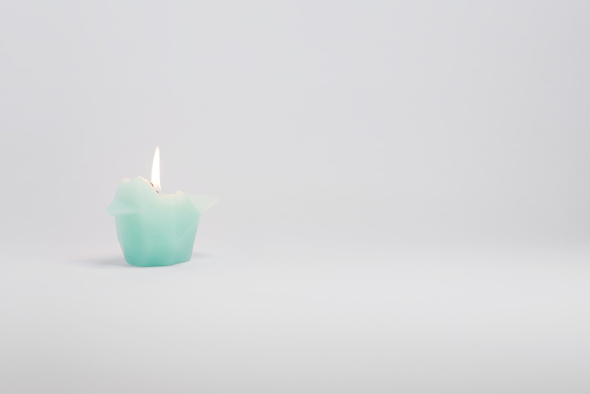 Side view of mint bird shaped pyropet candle that has a burning wick. 