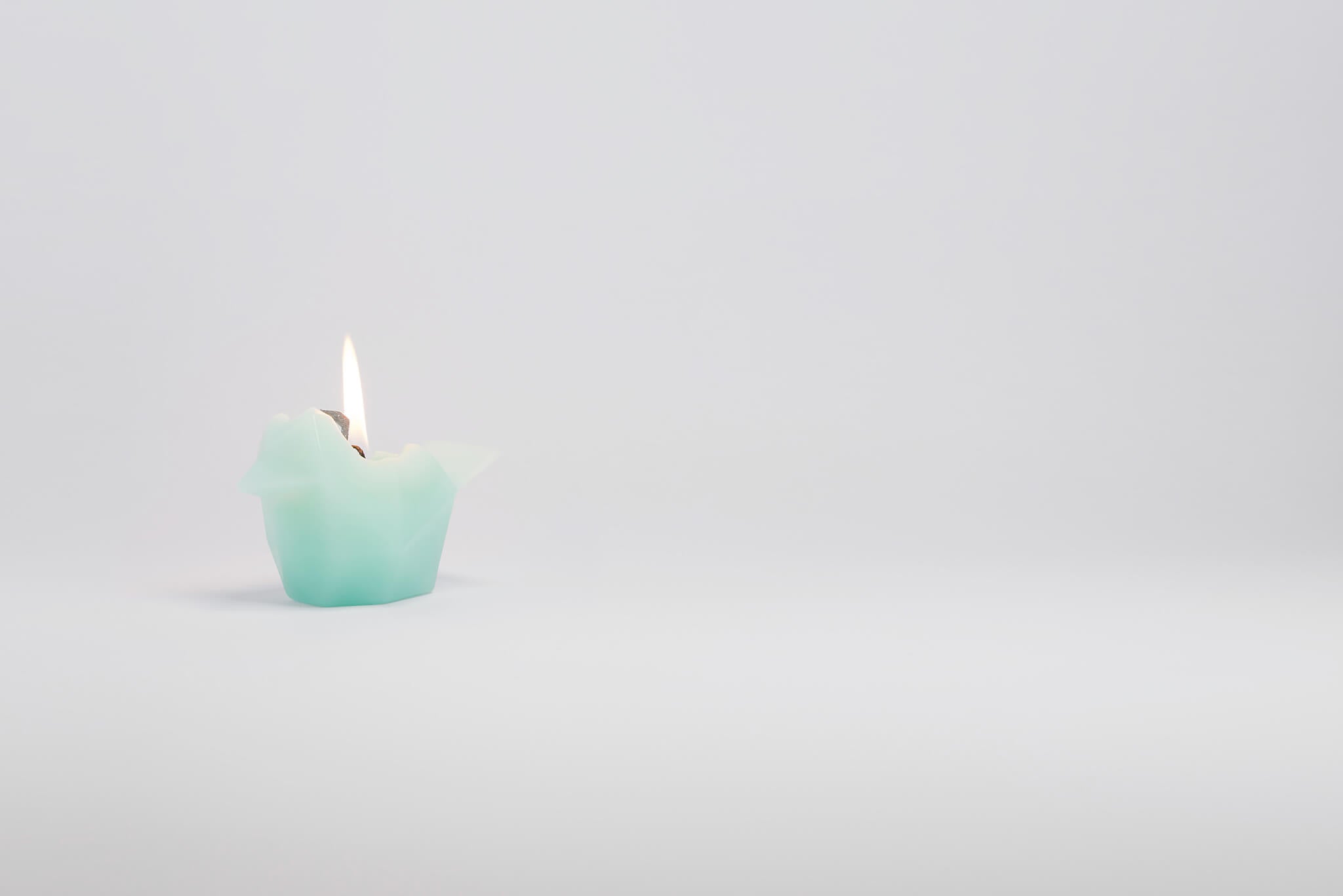 Side view of burning mint bird shaped candle. As the wax melts a metal skeleton frame is revealed. 