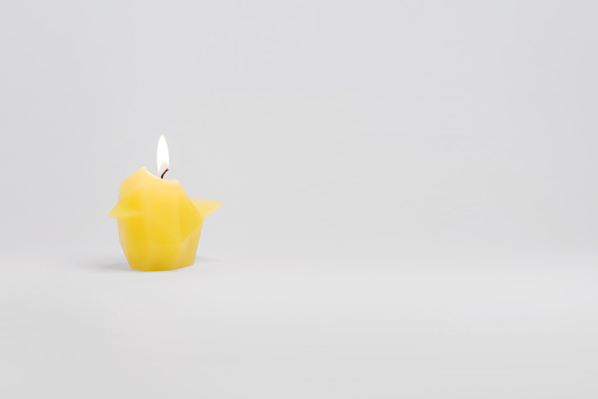 Side view of vibrant yellow bird shaped pyropet candle that has a lit wick. 
