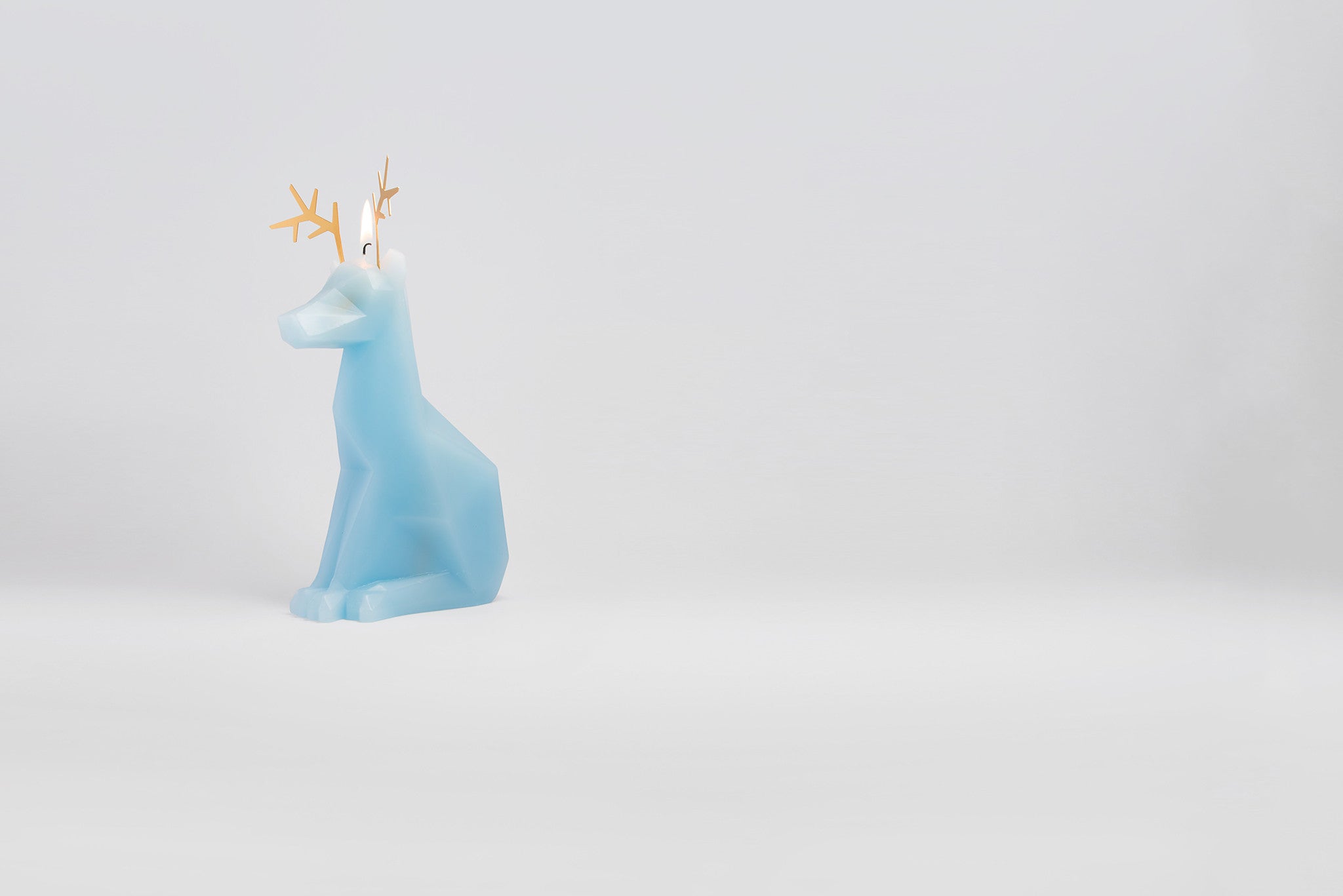 Side view of light blue dyri reindeer animal candle with the wick burning.