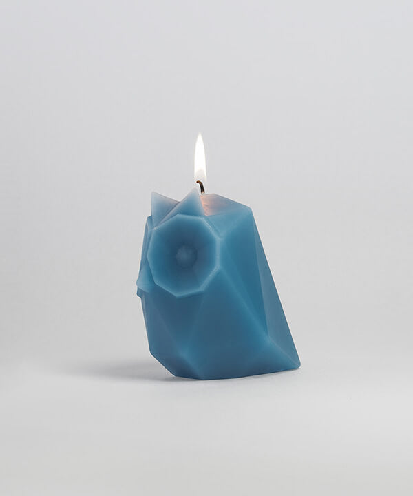 Side view of grey blue the owl shaped pyropet candle with wick burning.