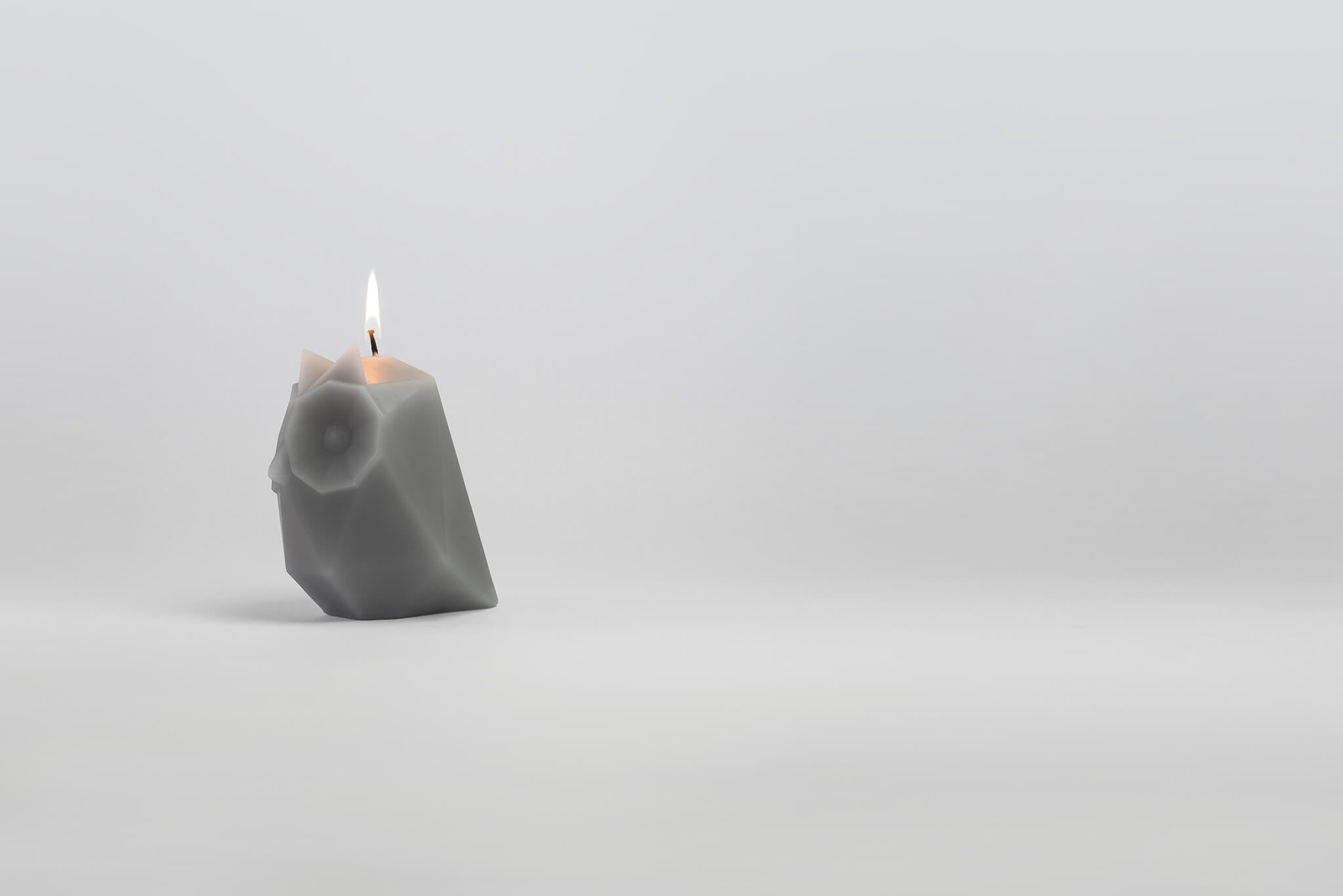 Side view of grey ugla the owl shaped pyropet candle with wick burning.
